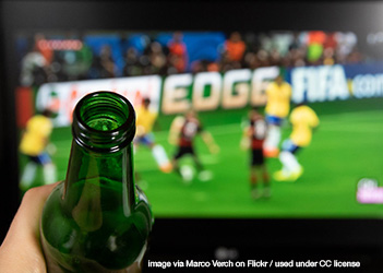 a beer bottle held up in front of a TV showing a soccer game